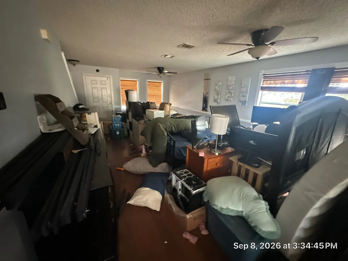 Before: cluttered front living area filled with furniture, boxes, and household items