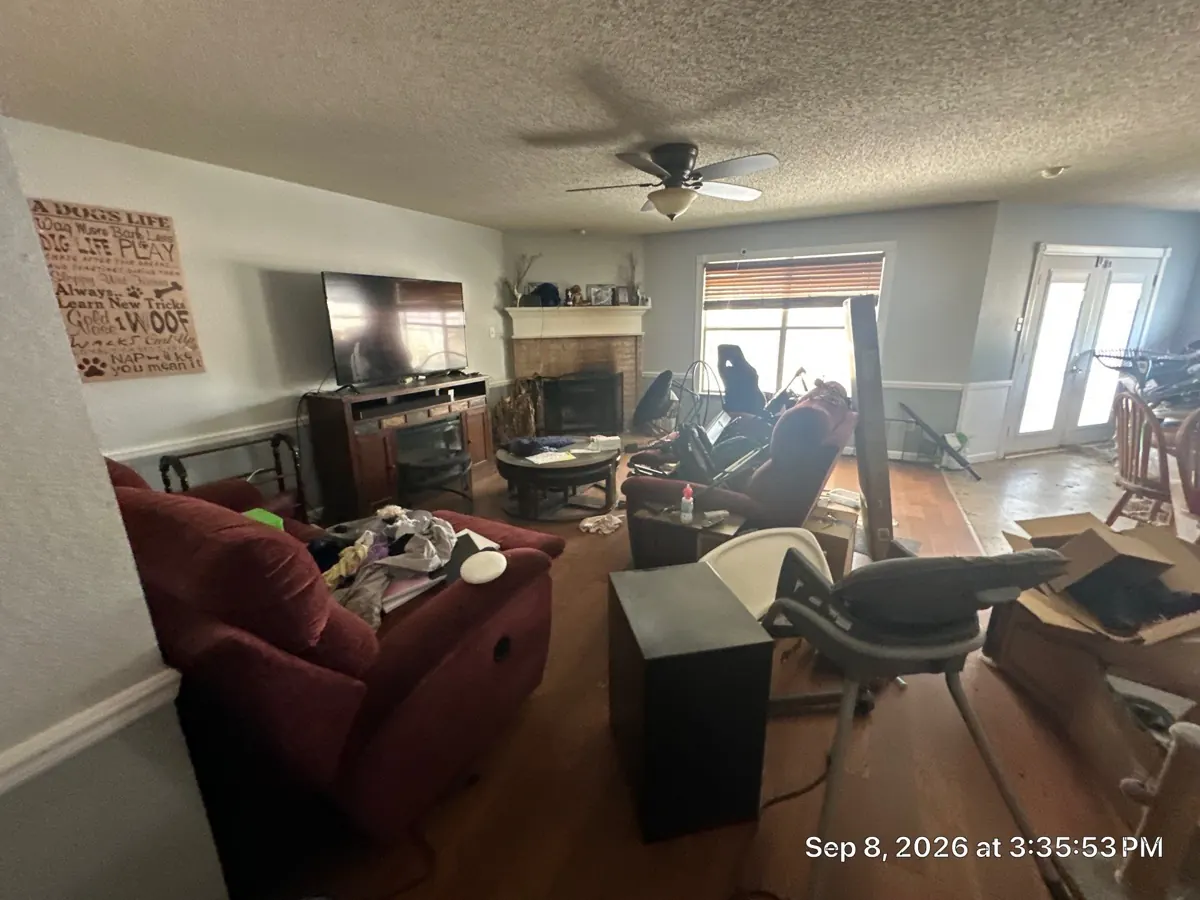 Before: cluttered living room with a corner fireplace filled with furniture, boxes, and household items
